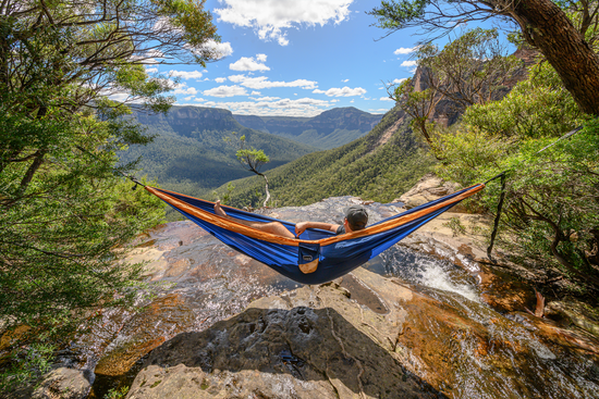 Man laying on River Blue Nakie hammock on a cliff with mountain view