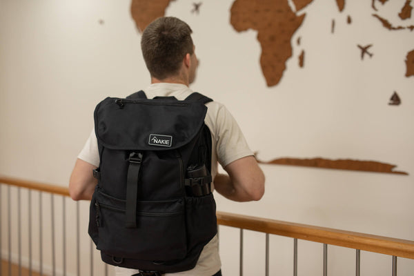 Black recycled travel backpack with flap closure, side pockets, and branded label, worn on back view.