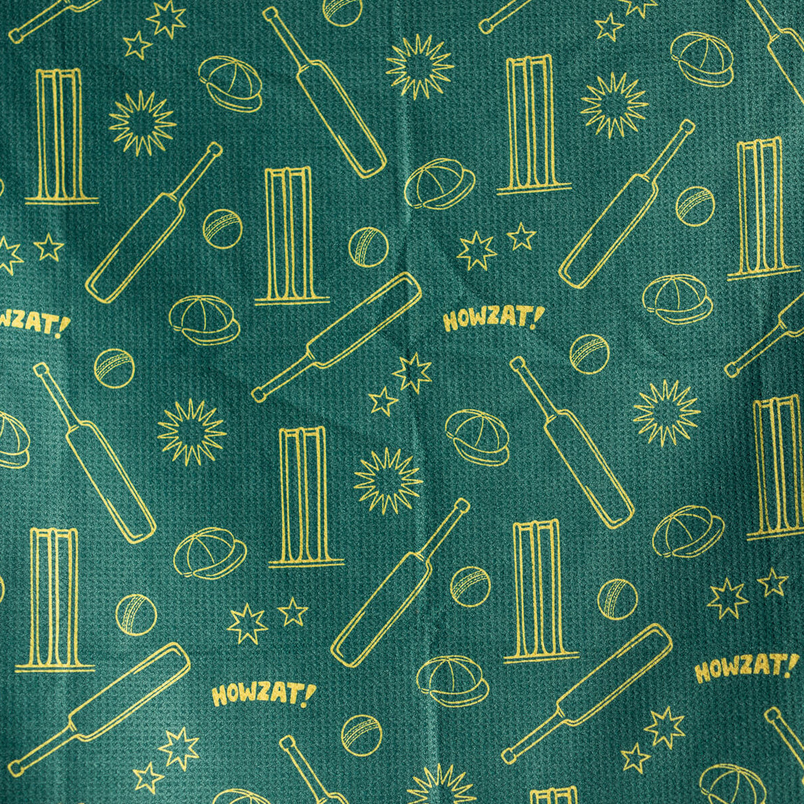 Teal beach towel with gold cricket-themed pattern including bats, stumps, balls, planets, stars, and HOWZAT! text