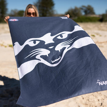 Navy beach towel with white striped Geelong Cats AFL logo design, sand-free fabric, held on sandy beach