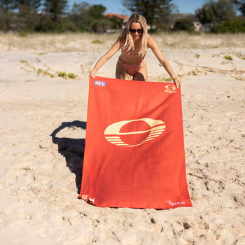 Gold Coast SUNS recycled sand-free beach towel in red with cream logo, displayed on beach.