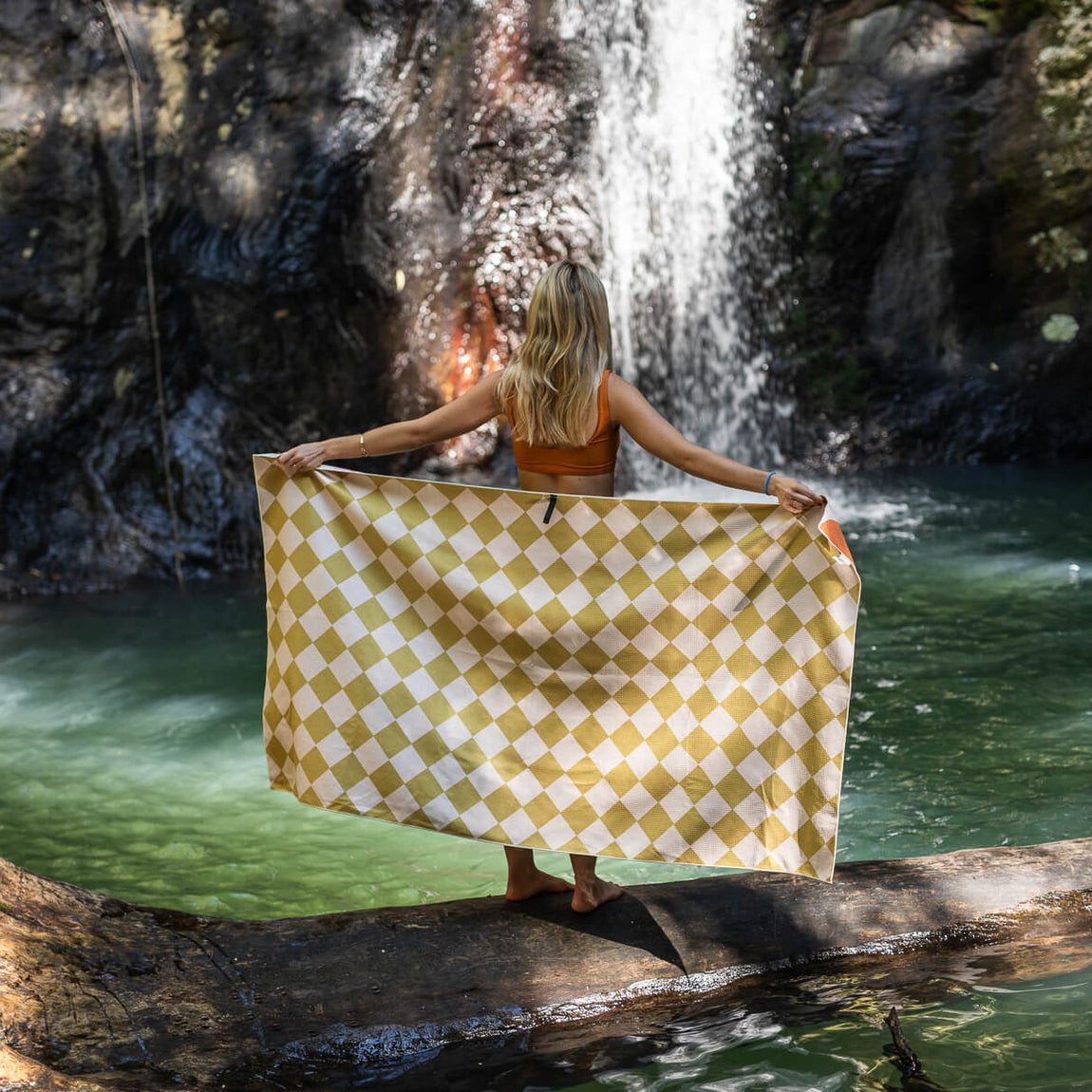 Gold and cream diamond-patterned recycled beach towel held open by woman at waterfall