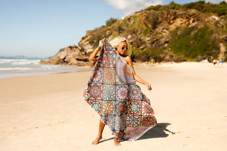 Image of a woman holding Nakie's recycled sand-free beach towel in one hand, showcasing the lightweight and portable design for easy carrying.
